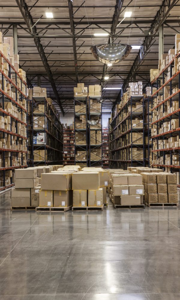 View down aisles of racks holding cardboard boxes of product on pallets  in a large distribution warehouse